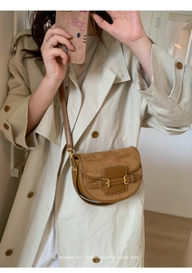 Detail view of a vintage brown suede saddle bag with metal buckles on a crossbody strap