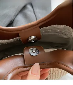 Details des silbernen Magnetverschlusses und braunem Lederbesatz an einer Strohtasche