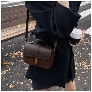Detail of dark brown retro crossbody bag with gold buckle and textured leather stitching