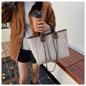 Detail of canvas tote bag featuring brown leather trim and metal chain strap in autumn setting