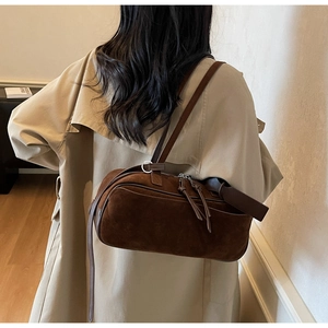 Close-up of deep brown suede shoulder bag with dual zippers and minimalist leather tassels