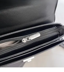 Close-up of the smooth silver zipper pull and interior compartment of the black leather bag