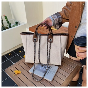 Detail of off-white canvas tote bag with brown leather trim and chain strap on bench