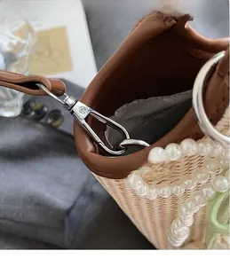 Detailaufnahme des Metall-Karabinerverschlusses und der Perlenkette an der gewebten Tasche