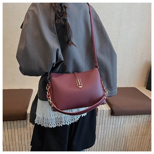 Detail of burgundy lychee grain leather crossbody bag with gold hardware and chain strap