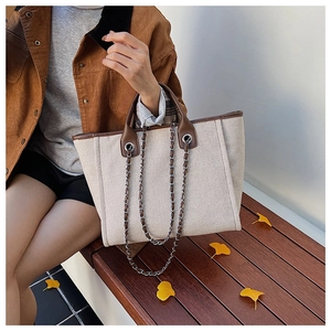 Detail of canvas tote bag with brown leather trim and metal chain straps on autumn bench