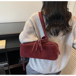 Detail of burgundy suede shoulder bag with long strap and tassel zipper on model