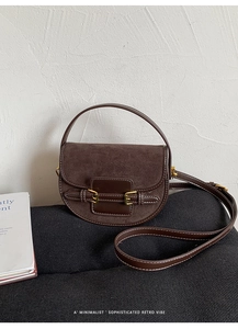 Detailed close-up of dark brown suede saddle bag with vintage golden buckles and leather