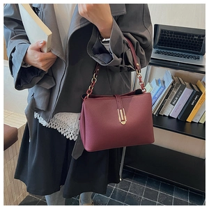 Close-up of burgundy lychee leather bag with gold buckle and chain strap on a desk