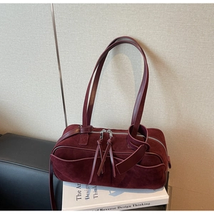 Detail view of burgundy matte suede shoulder bag with dual zippers and decorative tassels