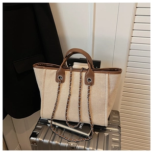Detail of beige canvas tote bag with brown PU handles on a silver suitcase