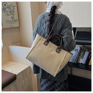 Beige canvas tote bag with brown leather trim and chain strap shown on a model