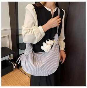 Close-up of grey plaid dumpling bag featuring drawstring details and a plush dog charm