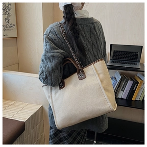 Detail of large canvas tote bag with brown leather trim worn by model in cozy interior