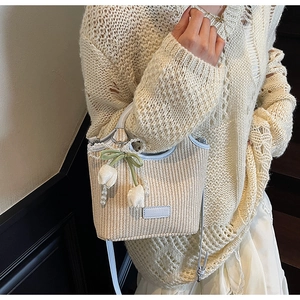 Detail der beigen geflochtenen Eimertasche mit blauem Lederbesatz und Tulpenanhänger