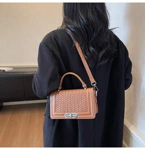Brown woven texture handbag detail with silver metal twist lock on a black blazer