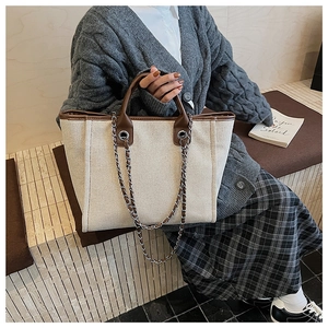 Detail of canvas tote bag with brown leather trim and silver metal chain strap