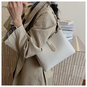Close-up of white shoulder bag with lychee texture and golden clasp on casual outfit