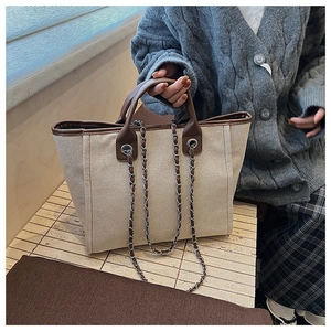 Detail of beige canvas tote bag featuring brown leather trim and silver metal chain strap