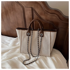 Detail of cream canvas tote bag with brown leather trim and metal chain strap