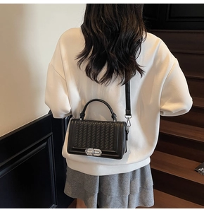 Detail of black woven texture shoulder bag with silver metal twist lock on the flap