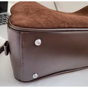Detail shot of brown shoulder bag bottom with protective metal studs and stitching