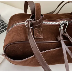 Close-up of matte brown suede texture and glossy silver hardware on a shoulder bag