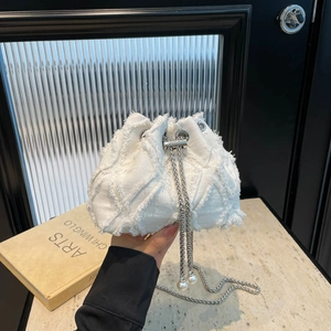 White denim bucket bag with frayed quilted texture and pearl chain strap on marble surface