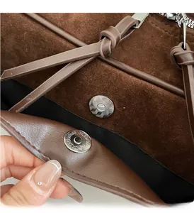 Close-up of silver magnetic closure and polished hardware on brown suede handbag