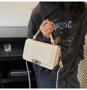 Close-up of cream crossbody bag featuring woven texture flap and silver swivel lock detail