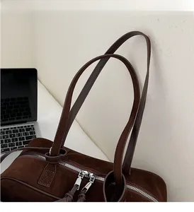 Close-up of a dark brown suede tote bag featuring durable double zippers and long handles