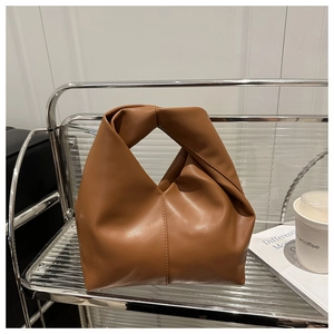 Detail of caramel brown handbag showing knotted handle craftsmanship and matte leather texture
