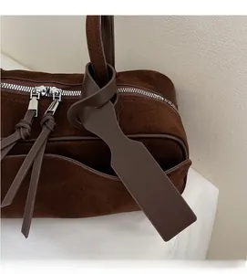 Detail of dark brown frosted suede handbag showing dual metal zippers and leather pulls