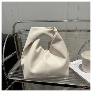 Close-up of cream leather dumpling bag with twisted handle on a modern glass shelf
