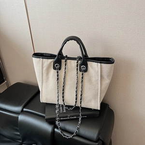 Minimalist cream canvas tote bag with black leather trim and chain strap on a seat