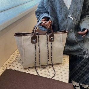 Large beige canvas tote bag with brown leather handles and decorative chain detail
