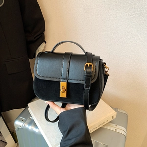 Minimalist black leather and suede crossbody bag with vintage gold buckle held by hand
