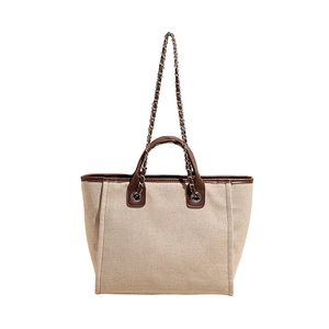 Large beige canvas tote bag with brown leather trim and chain strap on white background