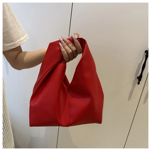 Detail of red ruched dumpling bag featuring an integrated knotted handle design