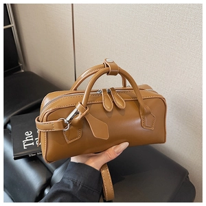 Close-up of brown leather handbag with silver hardware and dual handles being held