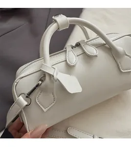 Detail of white leather barrel bag featuring double zip closure and metallic side hooks