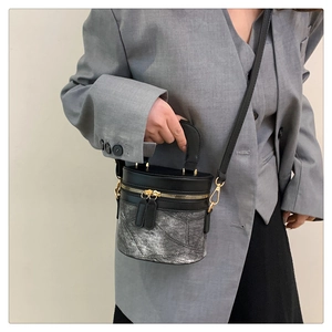 Detail der silbernen Metallic-Eimertasche mit schwarzem Ledergriff und goldener Hardware