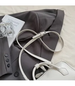 Detail of white leather shoulder bag with round handle and adjustable strap on a blazer