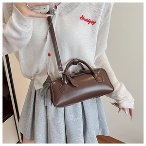 Detail of dark brown cylinder bag with top handles and adjustable shoulder strap