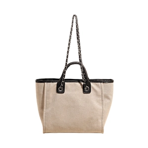 Large beige canvas tote bag with black leather trim and chain shoulder strap design