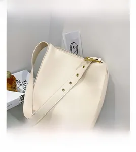 Detail of minimalist cream bucket bag showing wide adjustable strap and gold metal eyelets