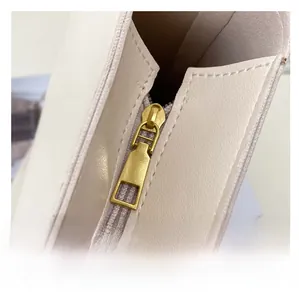 Close-up of a smooth golden metal zipper on a textured cream leather bucket bag