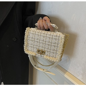 Close-up of white tweed handbag with pearl trim and golden clasp held by a model