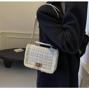 Detail of tweed shoulder bag with pearl trim and gold chain strap on model