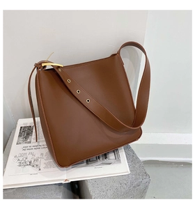 Detail of dark brown leather bucket bag featuring wide strap and golden metal eyelets